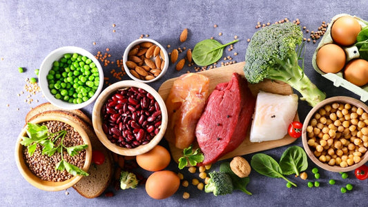 På bildet er det en masse ulike ingredienser, kjøtt, brokkoli, linser, bønner, potet, egg, erter, urter og fisk ligger på en trefjøl. Artikkelen handler om proteiner
